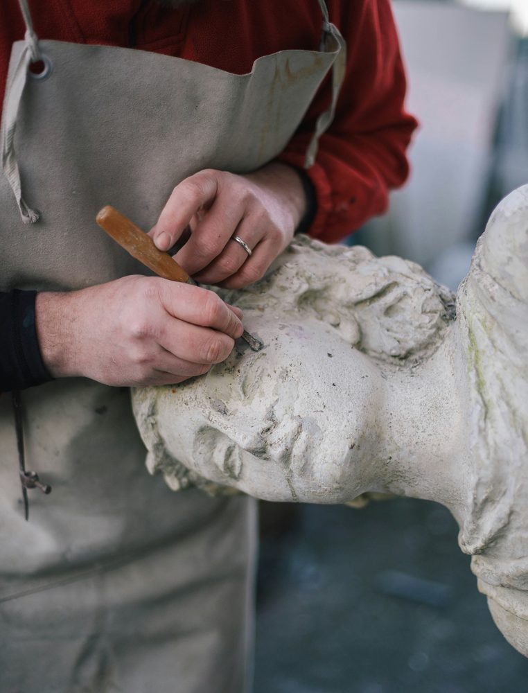 Conservator hand-carving detail into a weathered stone sculpture